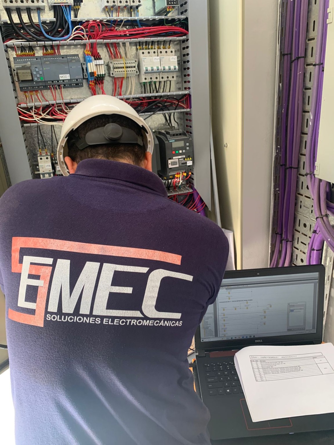 Técnico de Semec trabajando con una computadora frente a un tablero con PLC y variadores